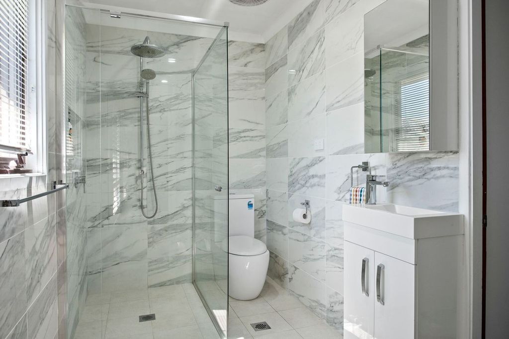 A modern bathroom with a glass-enclosed shower, a white toilet, and a marble-tiled wall.