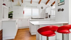 Uma cozinha moderna com armários brancos, uma ilha central, banquetas vermelhas e vigas de madeira no teto.