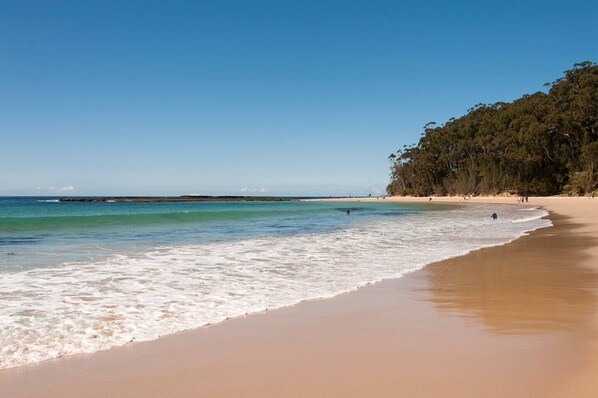 Enjoy a serene beach experience with calm waters and a picturesque backdrop of forest and rocky outcrops.