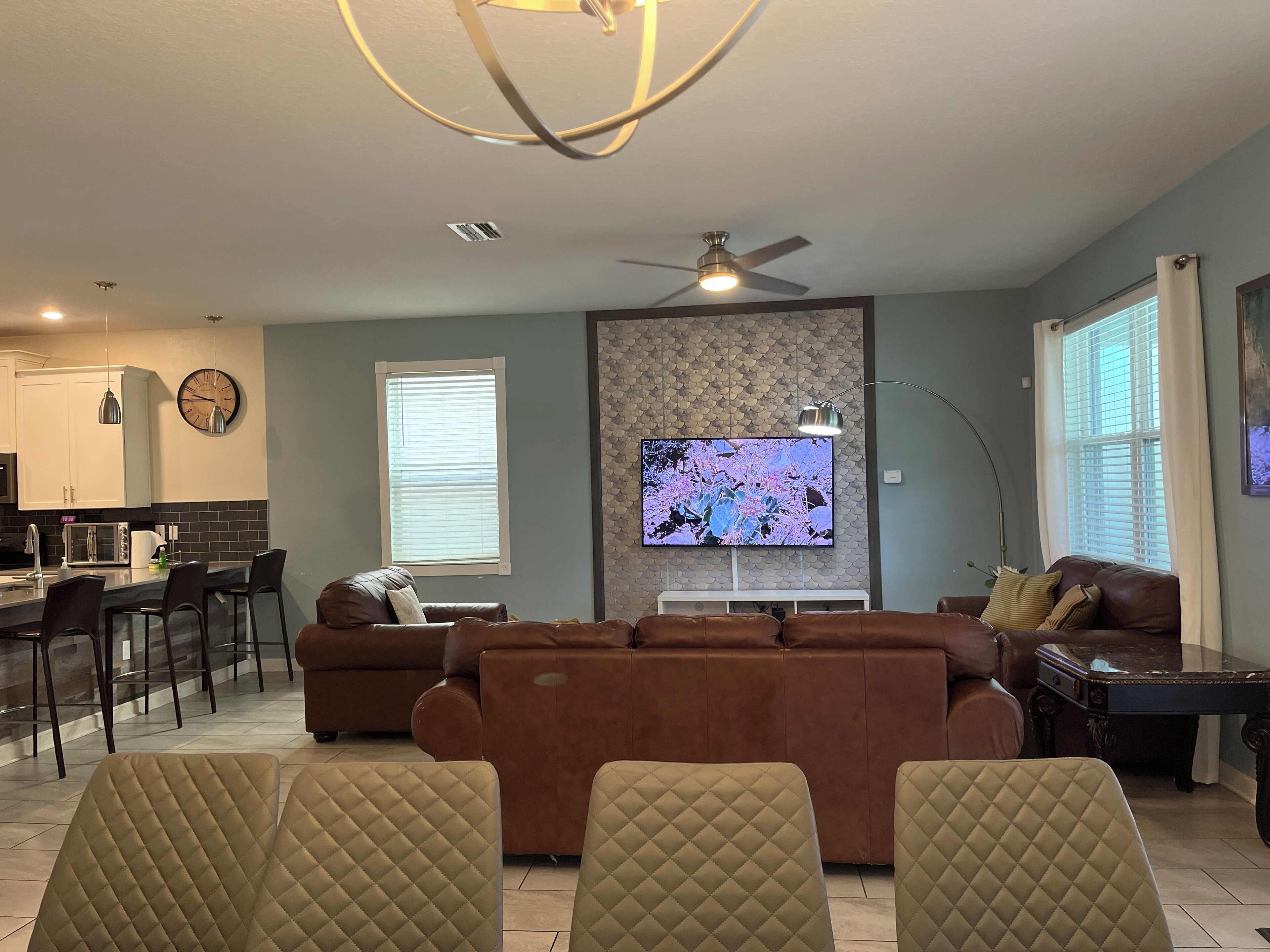 Una sala de estar moderna con un sofá marrón, un televisor montado en la pared y una zona de comedor con una cocina al fondo.