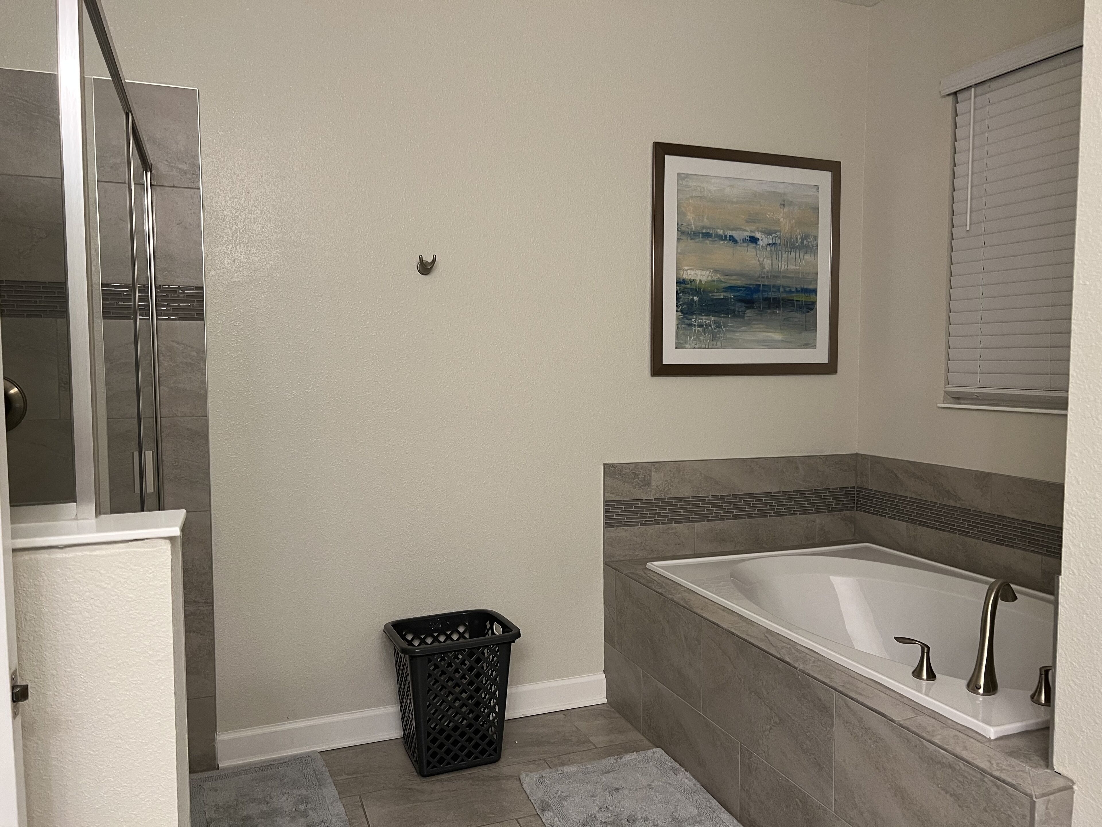 A bathroom with a bathtub, a shower, a framed picture on the wall, and a trash can.