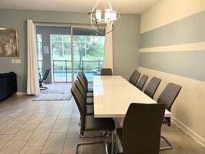 A conference room with a long table and chairs, a chandelier, and a view of a pool through large windows. - Vila 8BR Luxury near DISNEY with Pool, Spa, Free Parking, WiFi, (Reunion)