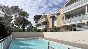 Una piscina con barrera de vidrio, rodeada por un edificio con balcones y cielo despejado.