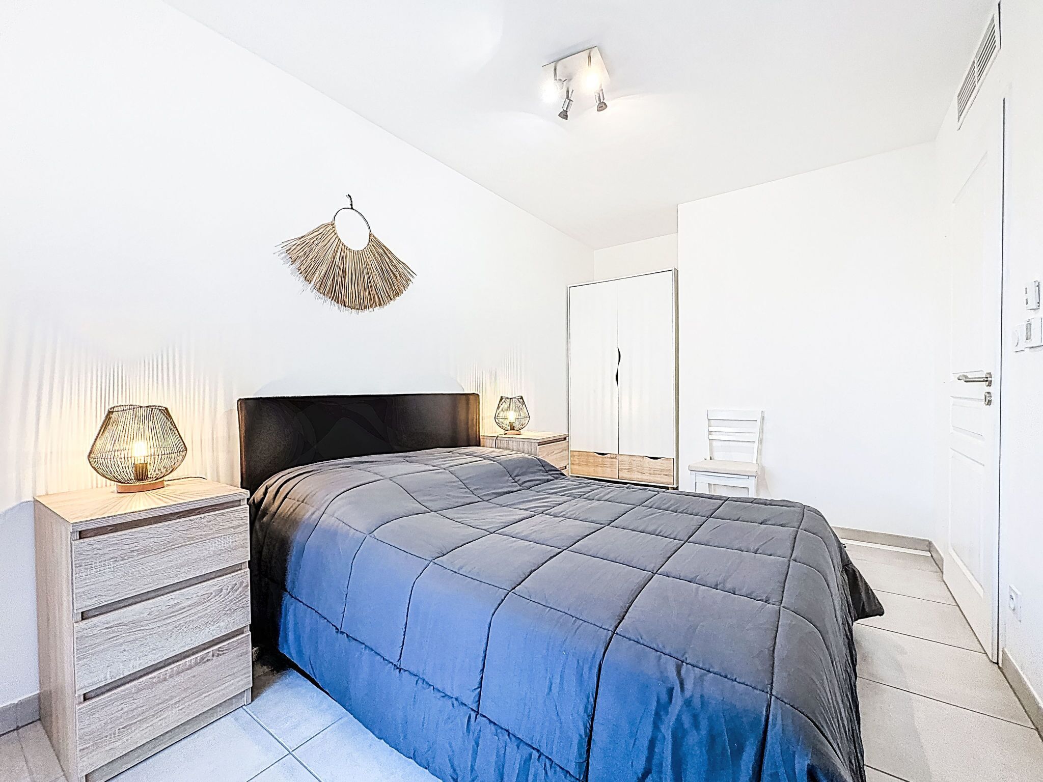 Un dormitorio con cama, mesitas de noche, armario y una lámpara colgante.