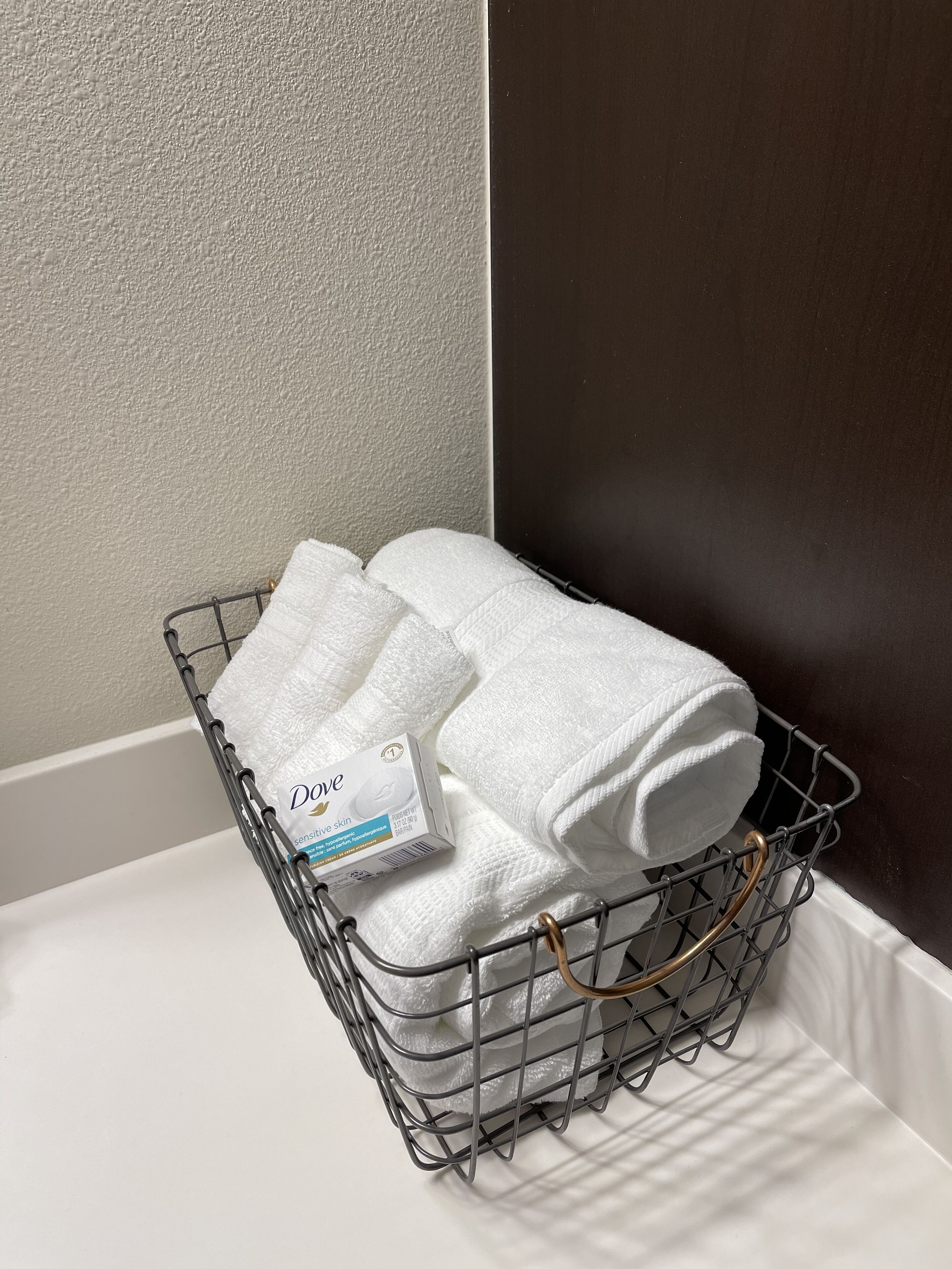 A metal basket with folded towels and a Dove sensitive skin product box on a white surface.