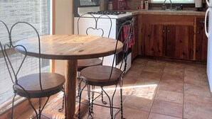 Une cuisine avec des meubles de rangement en bois, une cuisinière, un four à micro-ondes et un évier. Il y a une fenêtre avec des stores et une table avec des chaises.