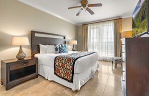A hotel room with a bed, two bedside tables with lamps, a ceiling fan, a large window with curtains, and a dresser. - Maui Resort Rentals: Honua Kai Konea 749, Premier 7th Floor Penthouse 3BR w/ Gorgeous Ocean and Black Rock Views! (Lahaina)