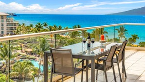 A balcony with a glass table, two chairs, a bottle of wine, and a candle. - Maui Resort Rentals: Honua Kai Konea 749, Premier 7th Floor Penthouse 3BR w/ Gorgeous Ocean and Black Rock Views! (Lahaina)