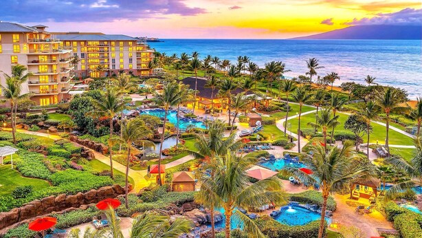 A resort with multiple swimming pools, palm trees, and a view of the ocean at sunset. - Maui Resort Rentals: Honua Kai Konea 749, Premier 7th Floor Penthouse 3BR w/ Gorgeous Ocean and Black Rock Views! (Lahaina)