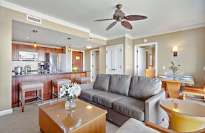 A modern kitchen with a microwave, stove, and bar stools. There is a gray leather sofa and a dining table with chairs in the living area.