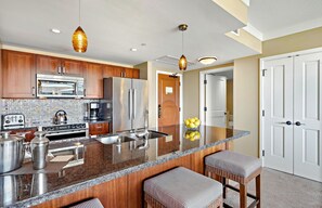 A modern kitchen with stainless steel appliances, a granite countertop, and a central island with bar stools.