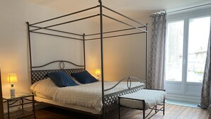 Ein Bett mit Baldachin, ausgestattet mit weißer Bettdecke und blauen Kissen, zwei Nachttische mit Lampen sowie ein Holzboden.