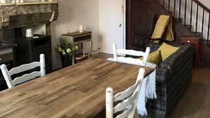 Ein Essbereich mit Holztisch, weißen Stühlen, Kamin, Treppe und einem karierten Sofa.