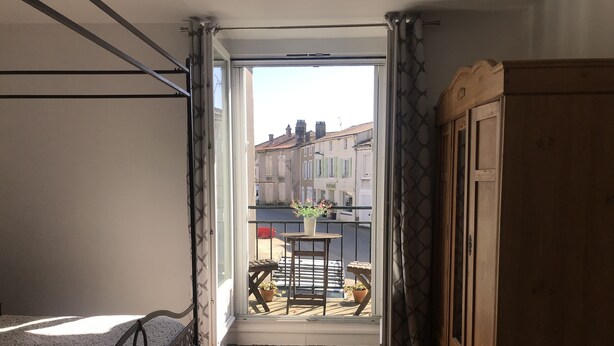 Ein Balkon mit Holzboden, einem kleinen Tisch mit Topfpflanze und Blick auf Gebäude im Hintergrund.