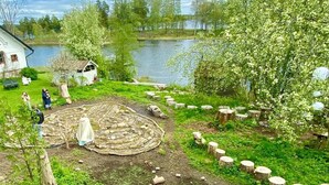 Una propiedad junto al lago con una estructura circular de piedra, un cobertizo pequeño y una casa blanca.