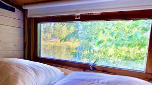 Una cama con sábanas blancas en una habitación con ventana que da a un paisaje natural.