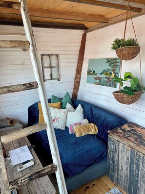 A cozy room with a blue sofa, wooden beams, a hanging plant, and a painting on the wall.