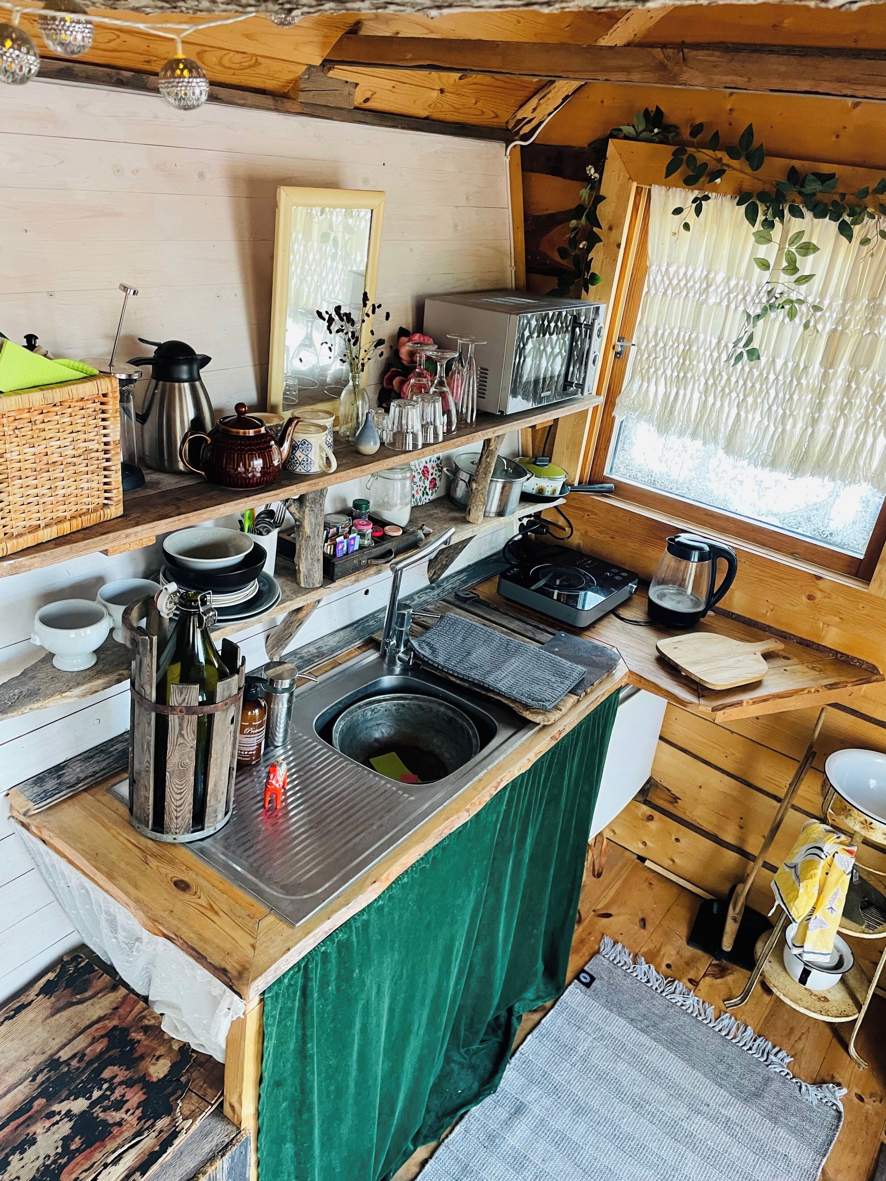 A compact kitchen with a sink, wooden shelves, and various kitchenware.