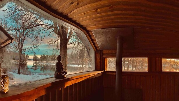 Interior de una cabaña con vistas a un paisaje nevado a través de un gran ventanal.