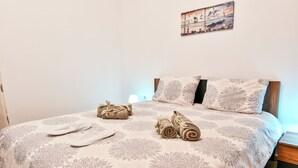 Ein ordentlich bezogenes Bett mit einem blumigen Überwurf, ein Paar weiße Hausschuhe und aufgerollte Handtücher.