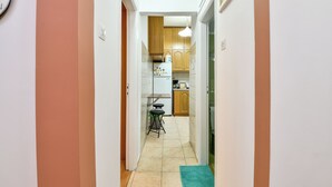 Eine schmale Küche mit Kühlschrank, Holzschränken und einem kleinen Tisch mit Hocker.