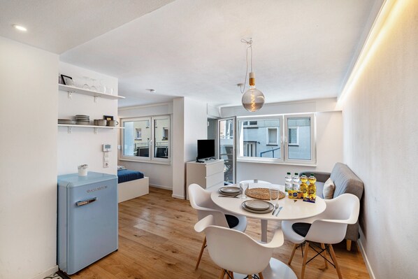 A compact kitchen with a blue refrigerator, white dining chairs, a round table, and a hanging light fixture.