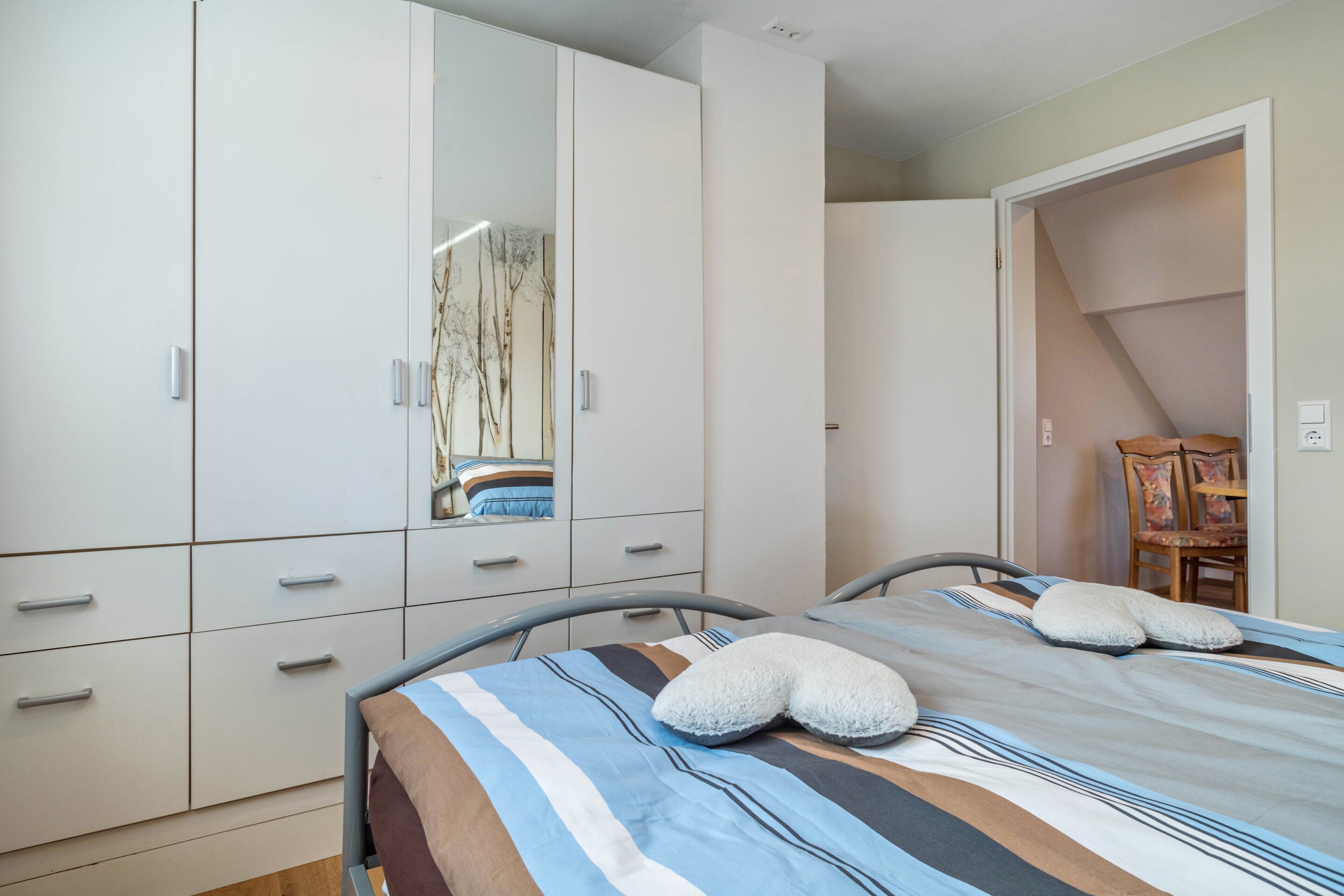 A bedroom with a bed, a wardrobe, a mirror, and a chair.