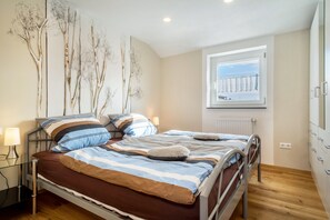 Une chambre à coucher avec un lit, des tables de chevet, une fenêtre donnant sur un paysage agréable et un radiateur.