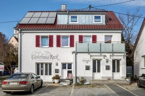 Un bâtiment à deux étages, doté d’une façade blanche, de volets rouges et d’une enseigne indiquant « Gastehaus Reck ».