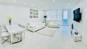 Una sala de estar moderna con un sofá blanco, una mesa de comedor de vidrio y un televisor de pantalla plana montado en la pared.