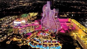 Un hotel con un edificio con forma de guitarra, varias piscinas y un área exterior bien iluminada.