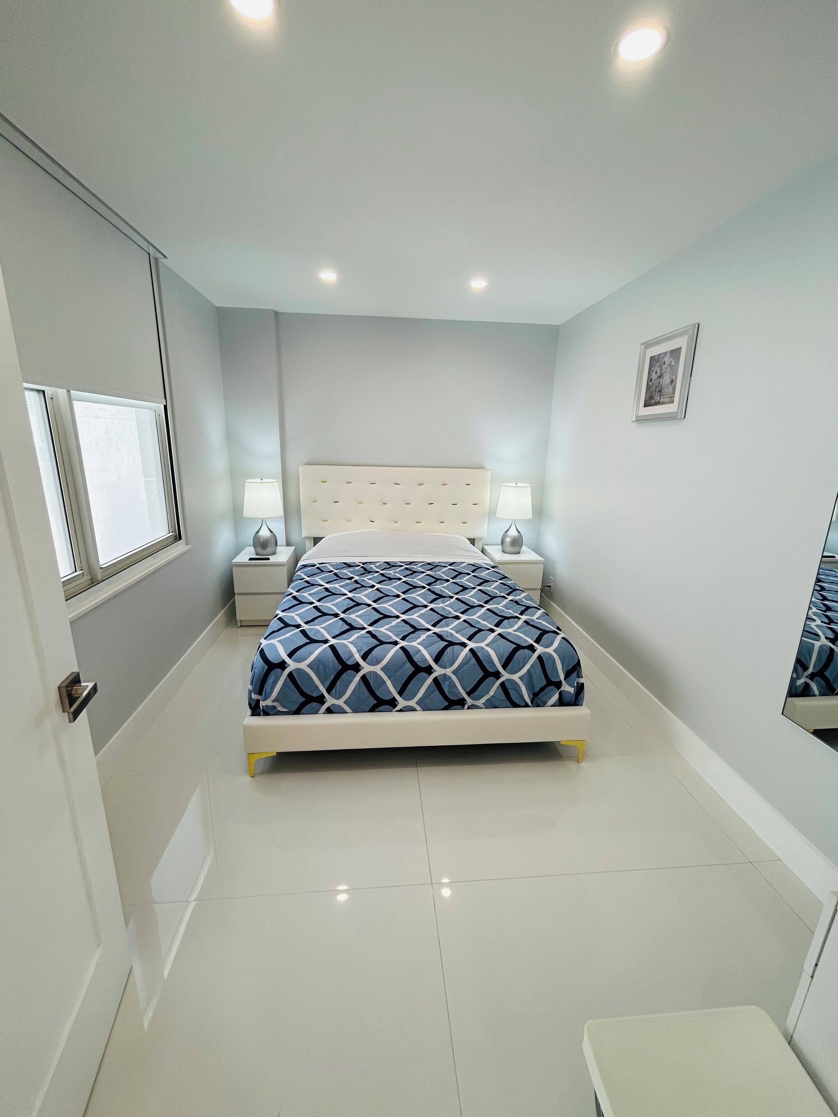A bedroom with a bed, bedside tables, a window, and a picture on the wall.