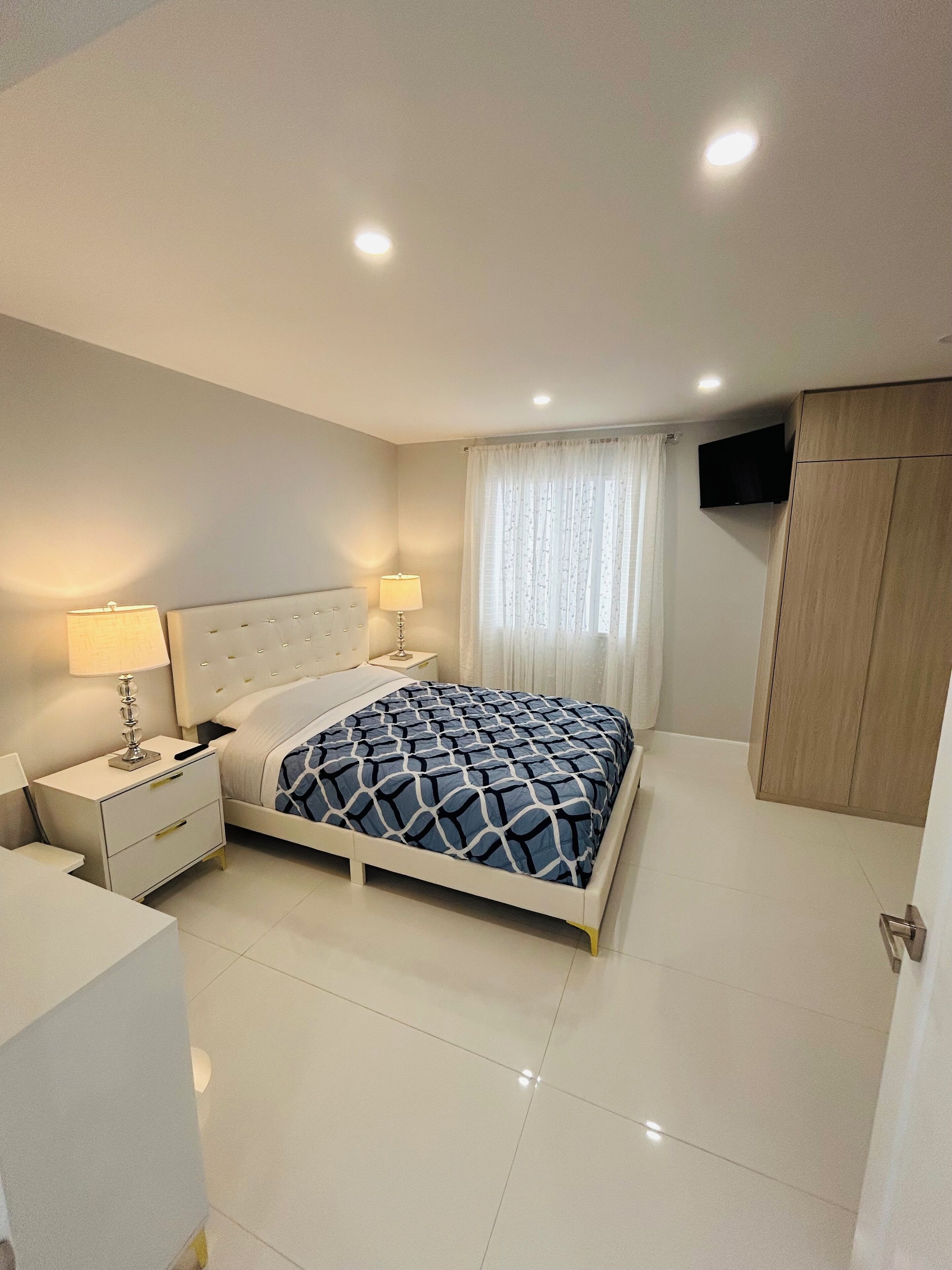 Une chambre à coucher moderne avec un lit, des tables de chevet, un téléviseur et une armoire.