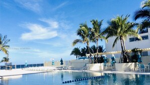 Una piscina con agua azul cristalina, rodeada de palmeras y sillas de descanso.