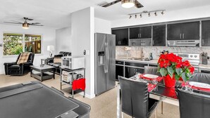 A modern kitchen with black cabinets, a stainless steel refrigerator, and a dining area with a glass table and black chairs. - Amazing salt water pool, patio, yard, laundry, kayaks, BBQ,hot tubprime location (Wilton Manors)