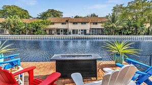 A poolside area with lounge chairs, a fire pit, and a view of a two-story building with a tiled roof. - Amazing salt water pool, patio, yard, laundry, kayaks, BBQ,hot tubprime location (Wilton Manors)