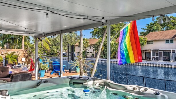 A hot tub area with a pool view, a covered patio, and a rainbow flag. - Amazing salt water pool, patio, yard, laundry, kayaks, BBQ,hot tubprime location (Wilton Manors)