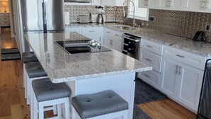 Una cocina moderna con armarios blancos, un refrigerador de acero inoxidable, microondas integrado y encimera de granito.