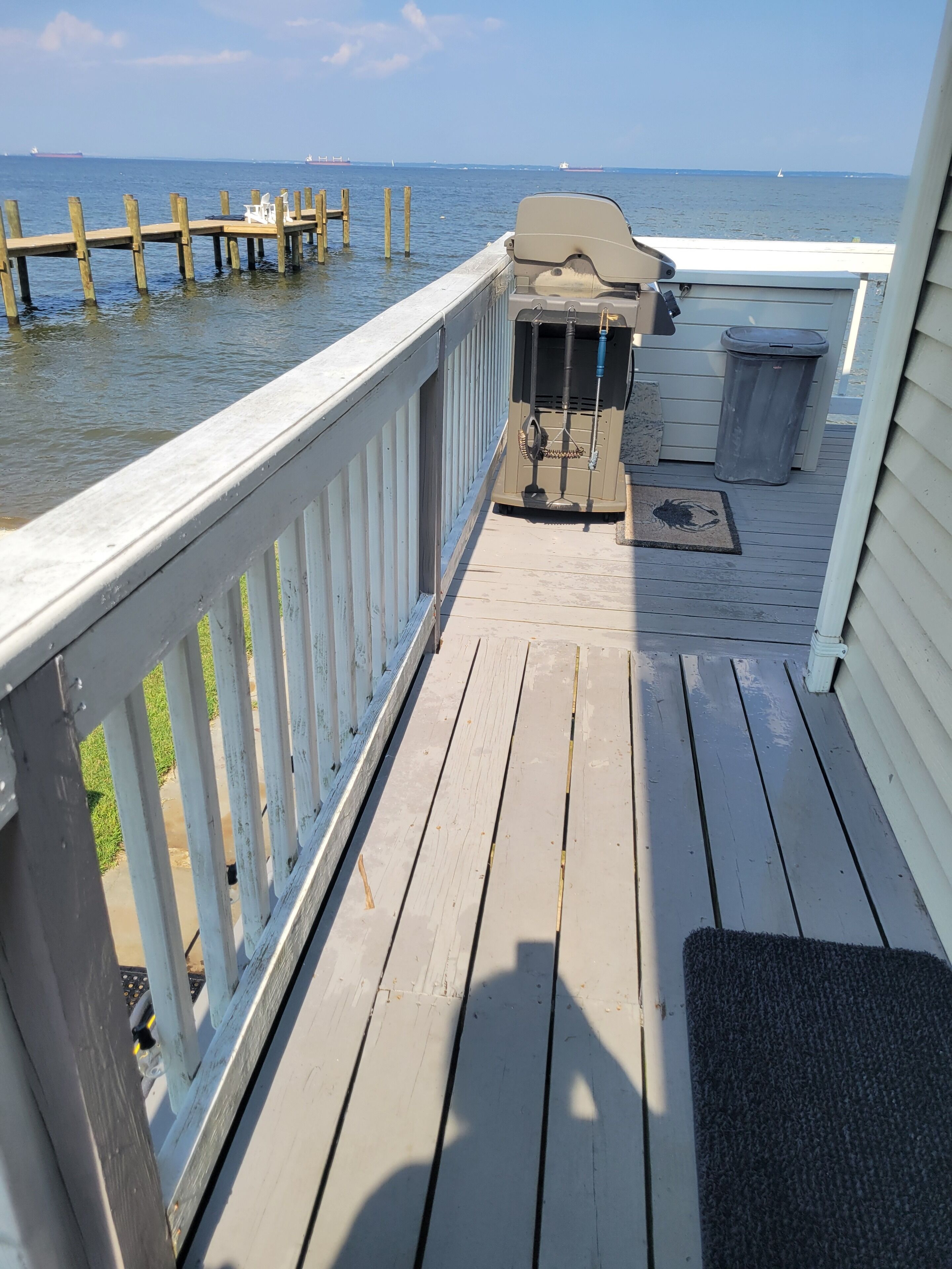 A wooden deck with a view of the water, a covered seating area, and a trash bin.