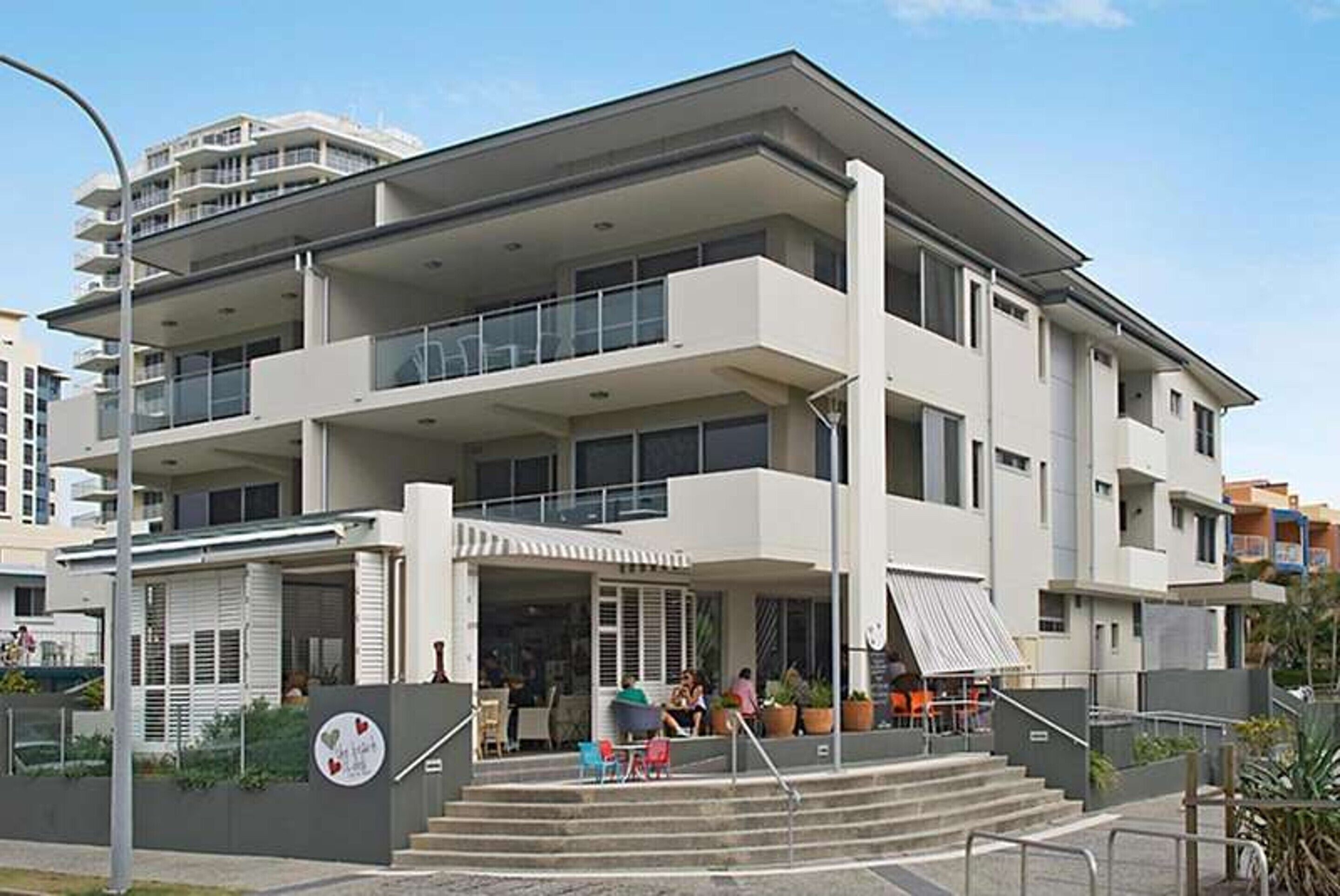 A multi-story hotel with a flat roof, balconies, and a covered outdoor seating area.