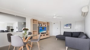 Ein modernes Wohnzimmer mit einem Glastisch, grauen Stühlen, einem grauen Sofa und einem Fernseher auf einem Holzboden.
