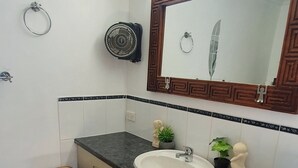 A bathroom with a wooden waste basket, a sink, and a mirror with a decorative frame. - Cotton Tree Tranquil Gem (Maroochydore)