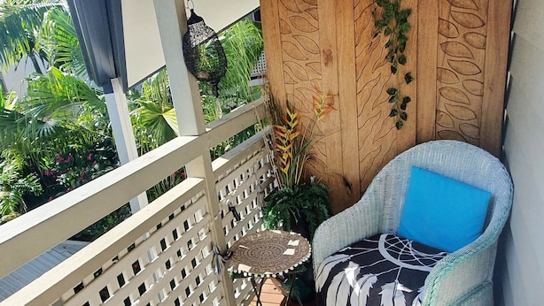 A wooden deck with a wicker chair and a small table, surrounded by a white lattice fence and lush greenery. - Cotton Tree Tranquil Gem (Maroochydore)