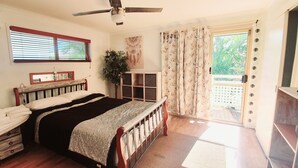 A bedroom with a bed, a ceiling fan, a window with blinds, a plant, a cabinet, and a sliding glass door leading to an outdoor area. - Cotton Tree Tranquil Gem (Maroochydore)