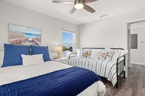 A bedroom with a large bed, two smaller beds, a ceiling fan, and a painting of a beach scene. - Relax in Style at your Private Pool & Hot Tub w Beach, Food & Drinks Nearby (Port St. Joe)