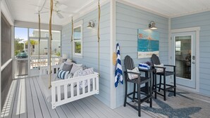 Een overdekt terras met een schommelzitje, een eethoek met stoelen, en uitzicht op de achtertuin.