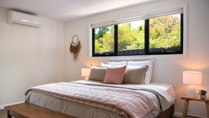 Une chambre à coucher comprenant un lit, une table de chevet, un banc, un appareil de climatisation, une fenêtre et des éléments de décoration murale.