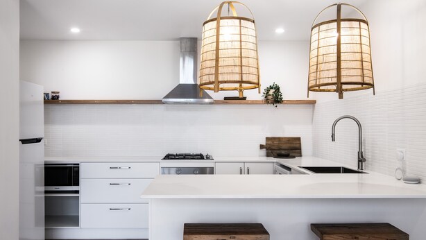 Une cuisine moderne avec des meubles blancs, un îlot central, deux tabourets en bois et des luminaires suspendus.