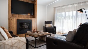 Un salon moderne doté d’un téléviseur à écran plat fixé à un mur en bois, d’une cheminée, d’un canapé confortable et d’une grande fenêtre ornée de rideaux légers.