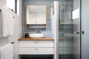 A modern bathroom with a white sink, wooden countertop, and a glass-enclosed shower.